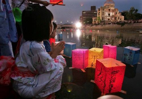 Behind her the dome ruins in Hiroshima.Japanese children in summer kimono offer prayers with paper lanterns..jpg